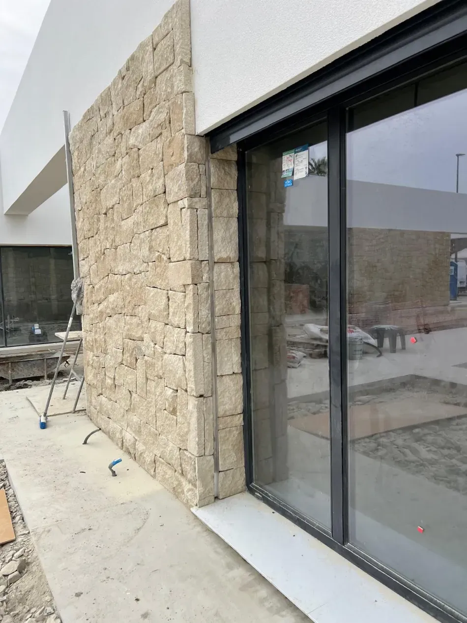 Muro de piedra junto a una moderna puerta corredera de cristal en una obra en construcción al aire libre.