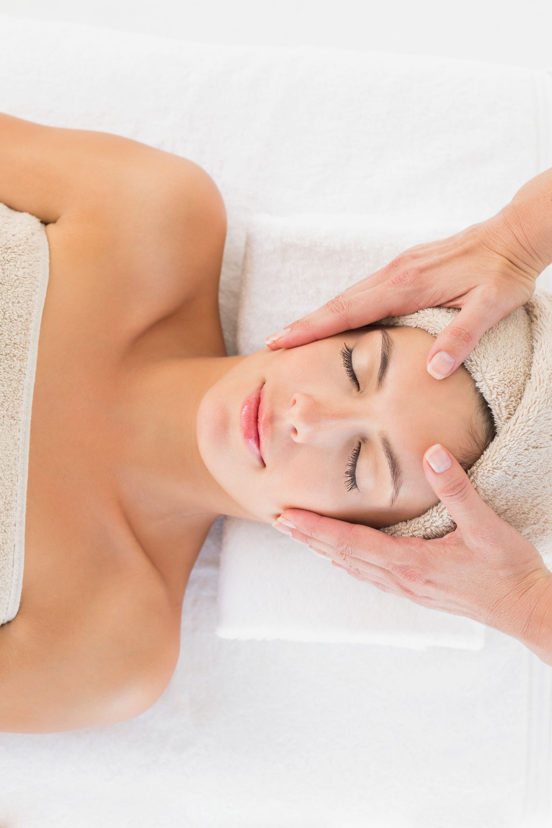 Femme recevant un massage du visage, les yeux fermés, sur une table de soins en spa