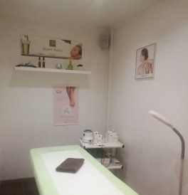 Salle de soins de spa avec une table blanche, des étagères, des serviettes et un portrait encadré au mur