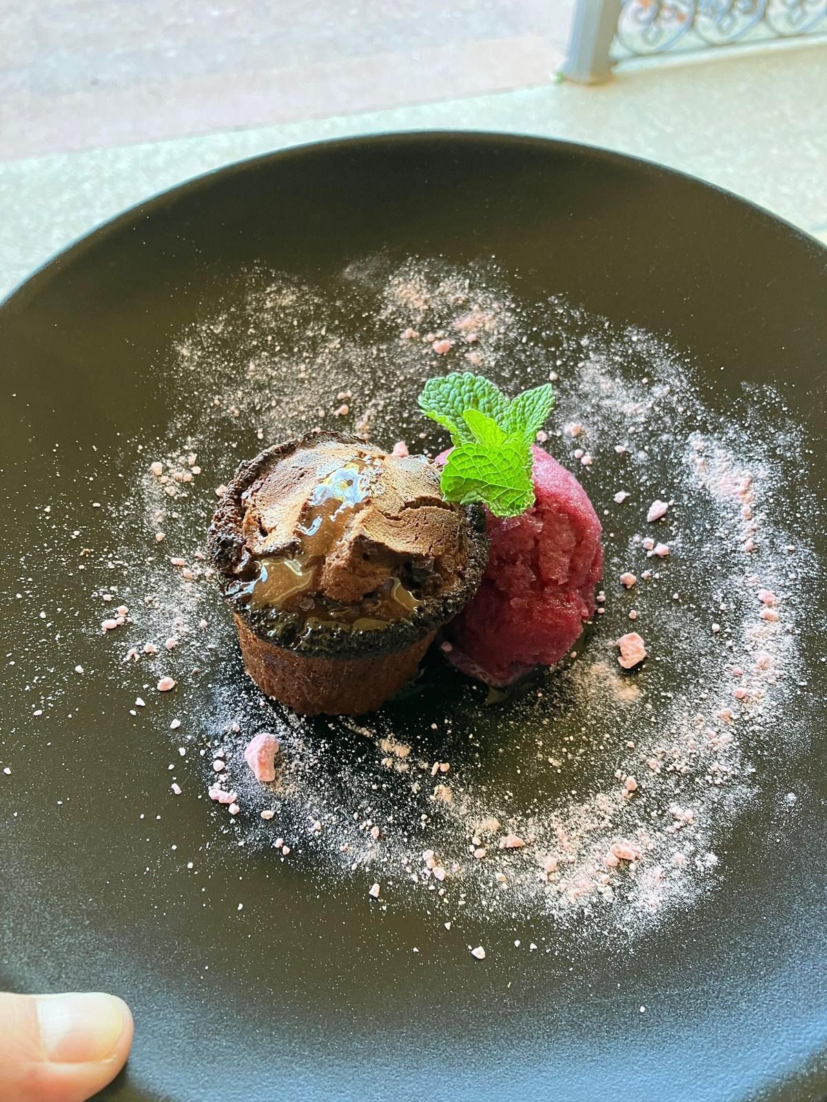 Una persona sostiene un plato negro con un postre encima.