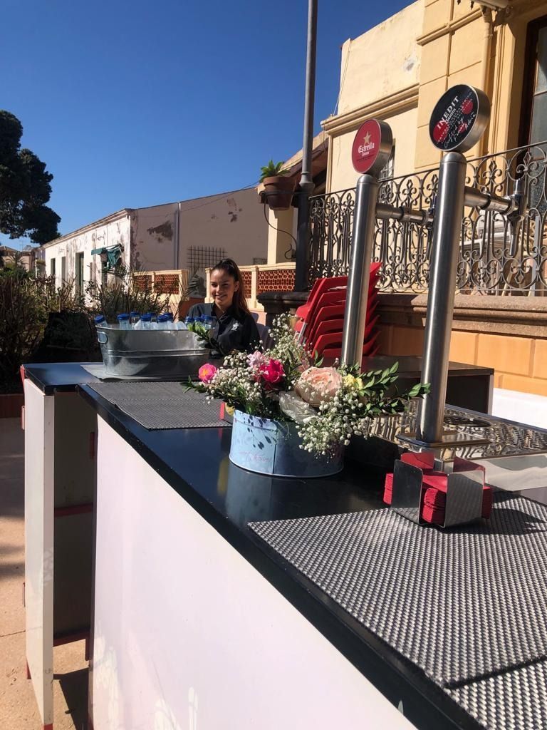 Una mujer está sentada en una mesa con flores frente a un edificio.