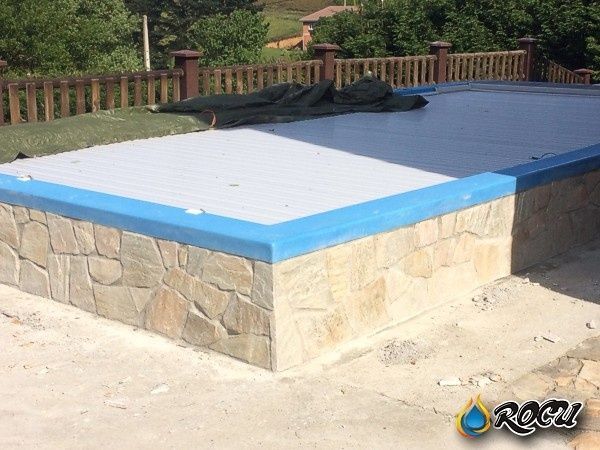 Piscina con pared de piedra y borde azul, cubierta por una cubierta blanca y verde.
