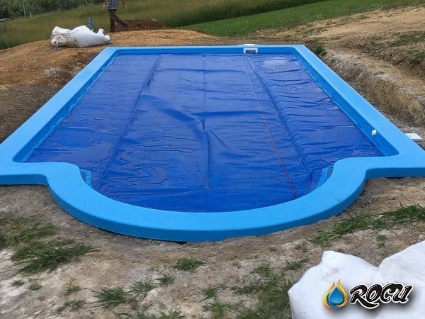 Piscina rectangular de color azul con cubierta azul, situada en una zona de tierra.