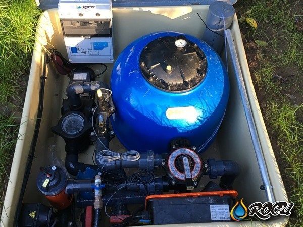Sistema de filtrado de piscina de color azul dentro de una caja de color beige, con diversas tuberías y maquinaria.
