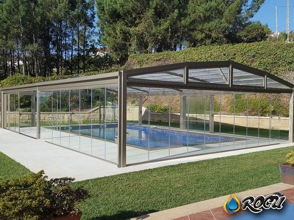 Piscina encerrada en una estructura de vidrio y metal en un patio trasero con césped.