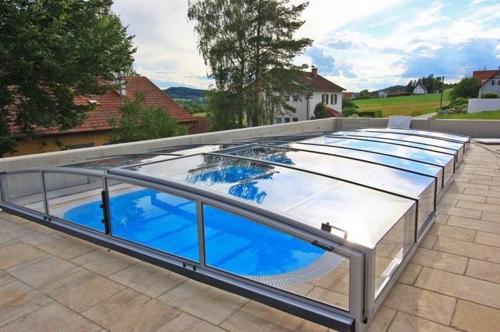 Cerramiento de piscina con techo transparente y retráctil sobre patio pavimentado.