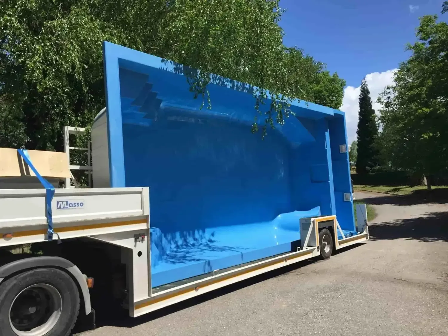 Carcasa de piscina rectangular de color azul sobre una plataforma de camión, al aire libre.