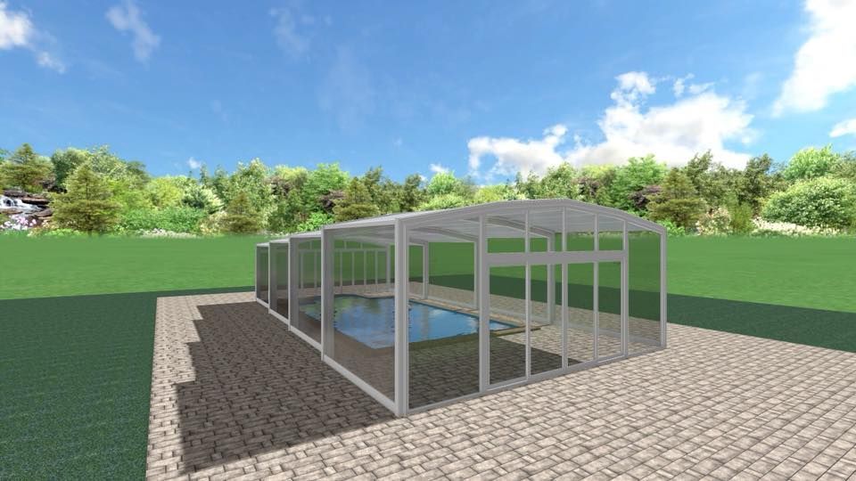 Recinto de piscina, paredes y cubierta de cristal, sobre patio de piedra, con árboles y cielo de fondo.