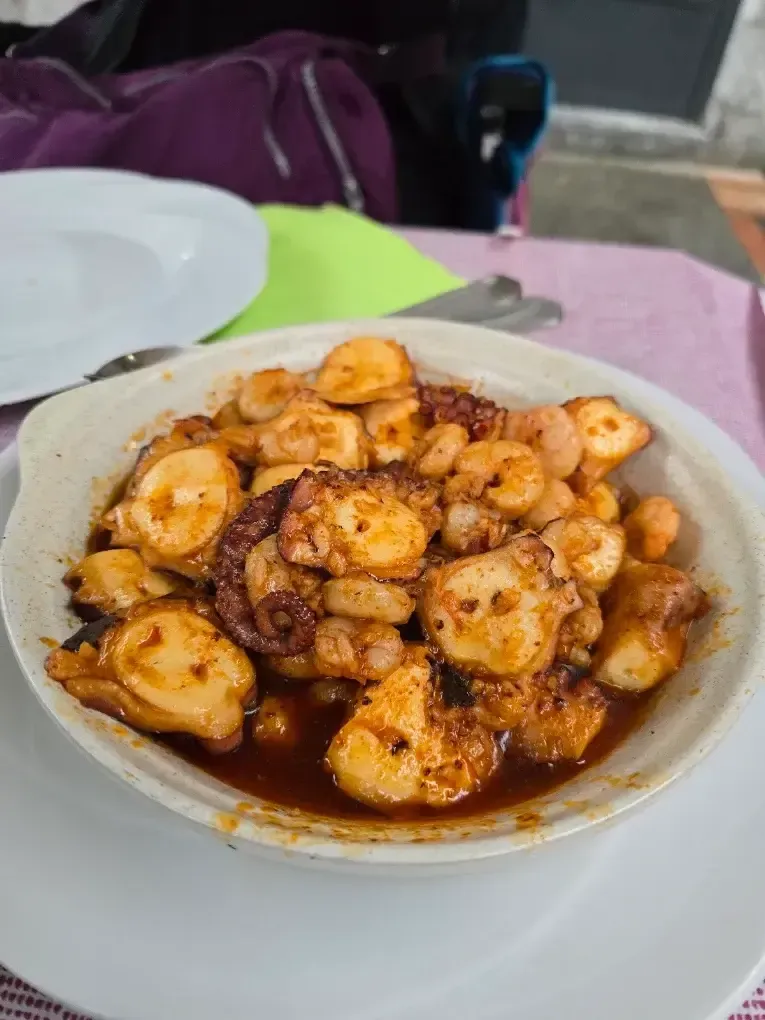 Un tazón de camarones en salsa con especias sobre una mesa, con utensilios y una bolsa morada al fondo.