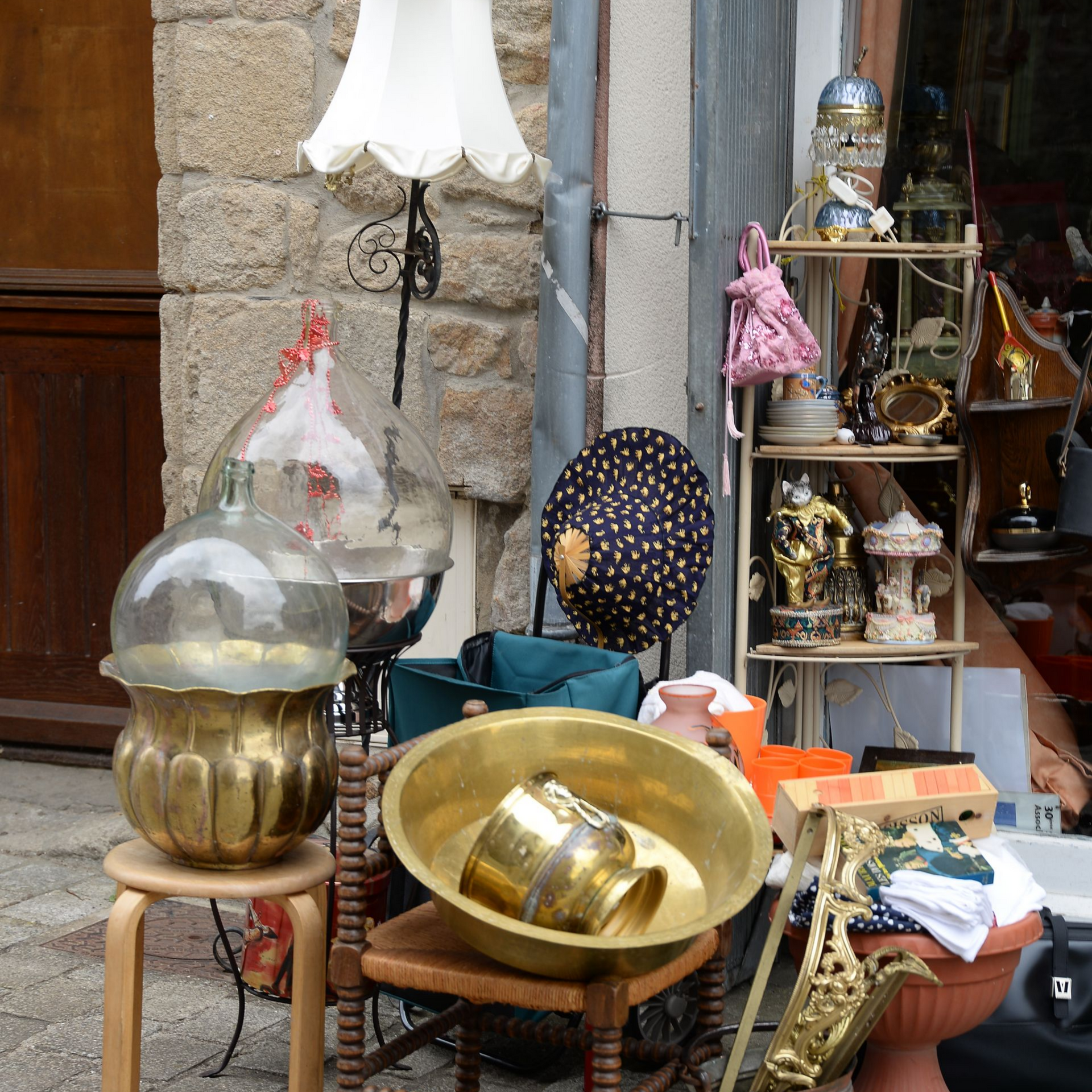 Étalon de marché aux puces en plein air : lampe, bol en laiton, étagères remplies de figurines et d’objets divers.