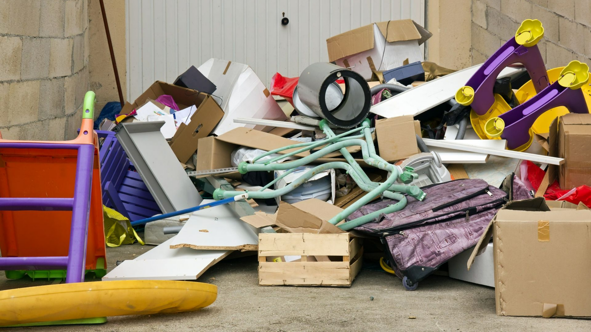 Tas de détritus : cartons, jouets cassés et autres débris devant un garage.