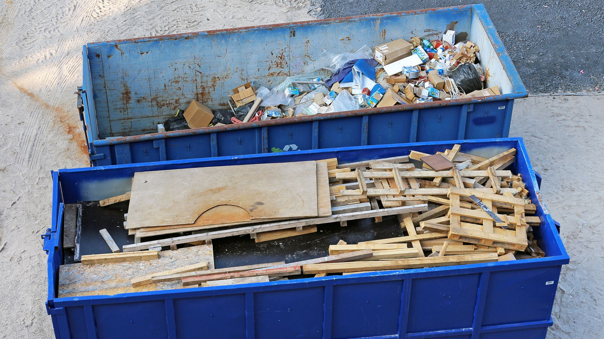 Deux bennes bleues remplies d'ordures et de débris de construction.