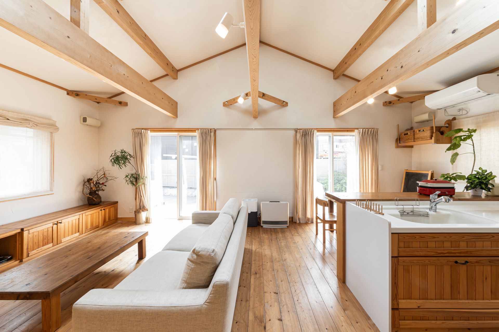 Espace de vie lumineux avec plafond voûté, poutres apparentes, parquet clair et cuisine.
