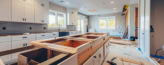 Rénovation de la cuisine en cours : armoires blanches, structure de l’îlot en bois, fenêtres et ustensiles sur les comptoirs.