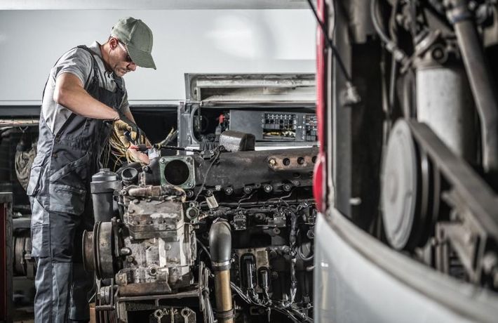Un hombre está trabajando en el motor de un autobús en un garaje.