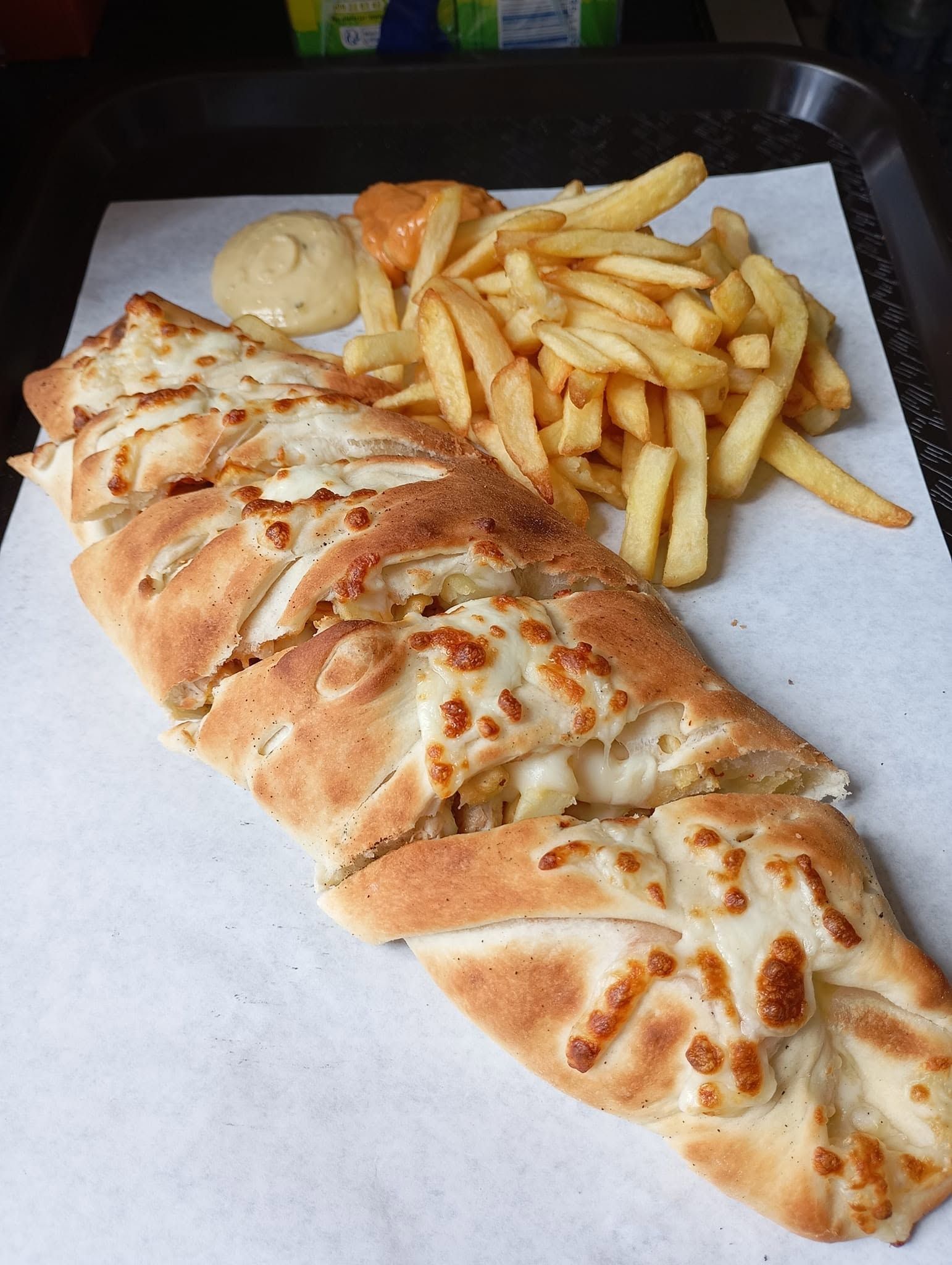 Pain grillé farci servi sur un plateau avec des frites et une petite sauce.