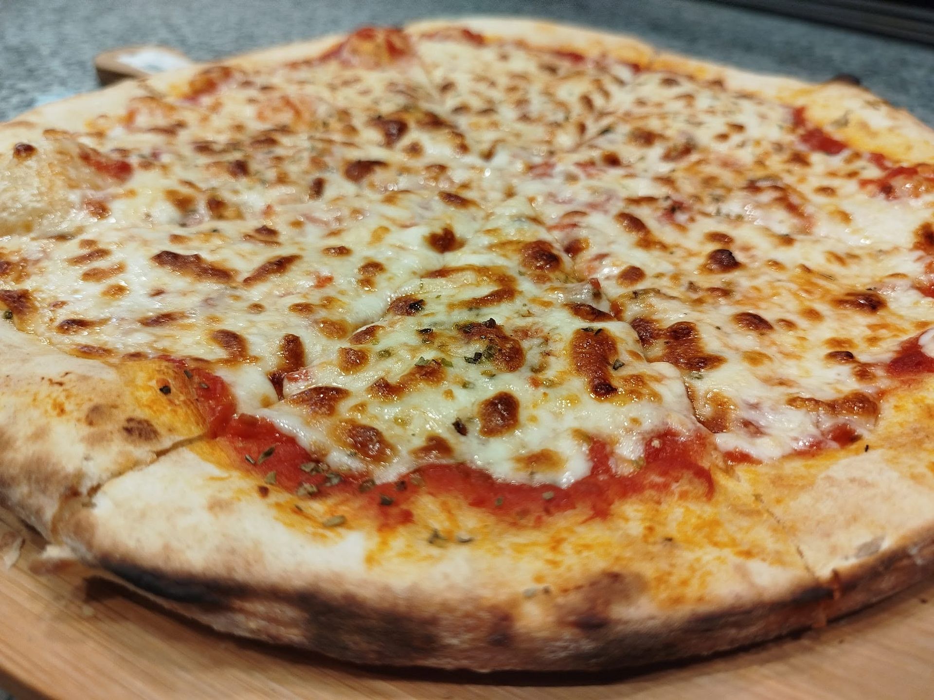 Pizza au fromage avec une garniture dorée et gratinée, servie sur une planche en bois.