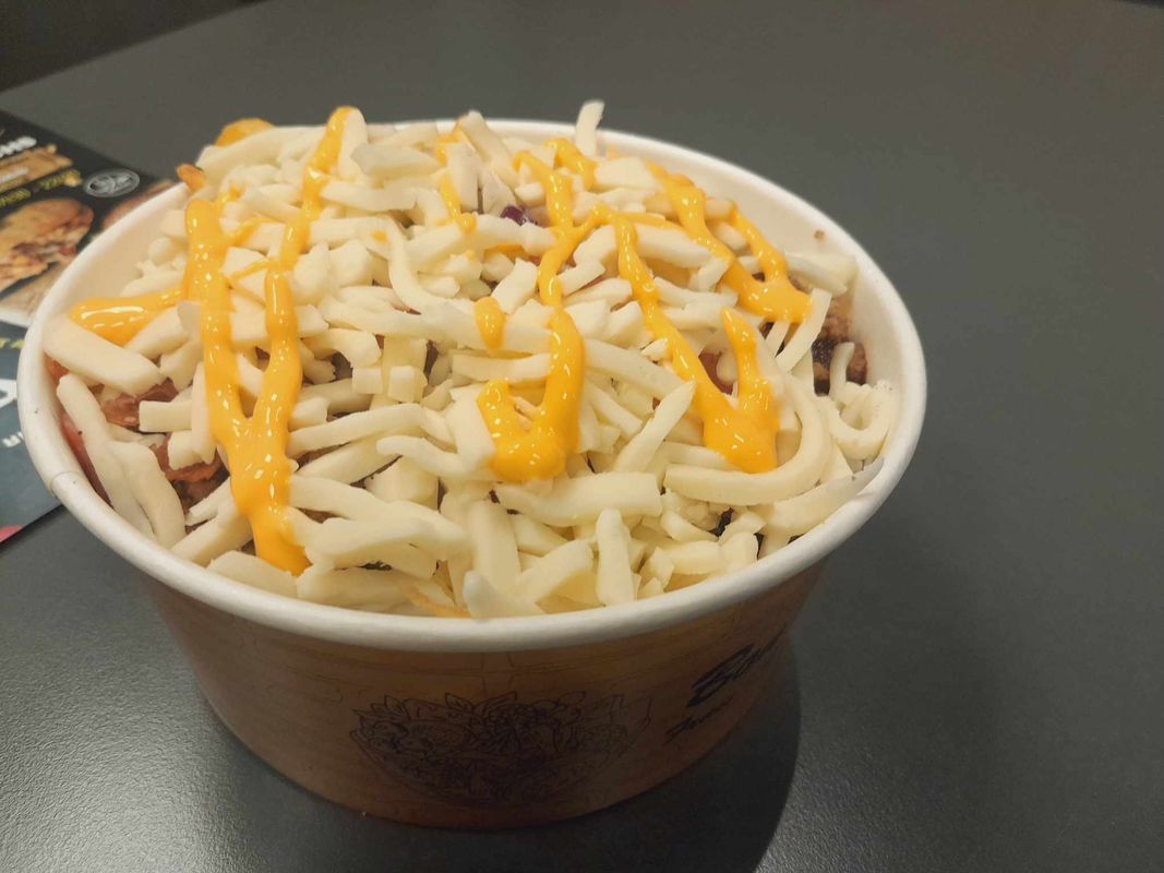 Une tasse de frites au fromage râpé nappées de sauce à l'orange, servie sur une table sombre.