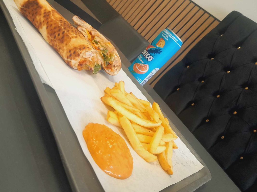 Wrap grillé, frites et sauce sur un plateau à côté d'une canette bleue sur une table de café