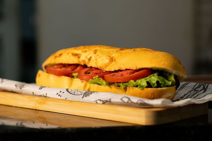 Sandwich sur une planche en bois, avec laitue et tomate dans un petit pain croustillant