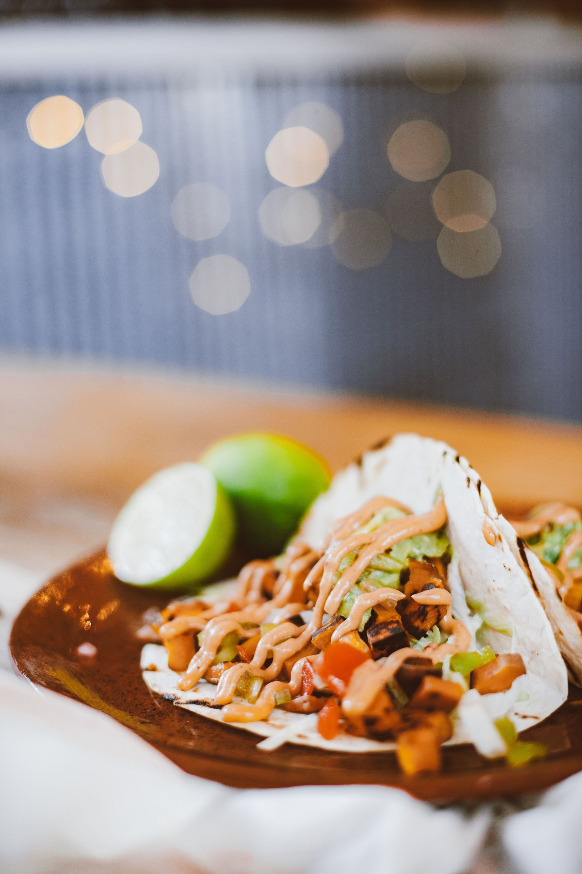 Tacos sur une assiette avec des quartiers de citron vert, présentés sur une table en bois avec des lumières floues en arrière-plan