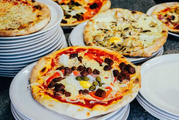 Assortiment de pizzas présentées sur des assiettes blanches empilées dans un buffet, avec des garnitures comme des olives, du fromage et de la sauce tomate.