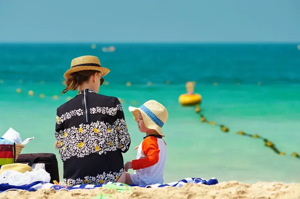 A woman and child are sitting on the beach looking at the ocean