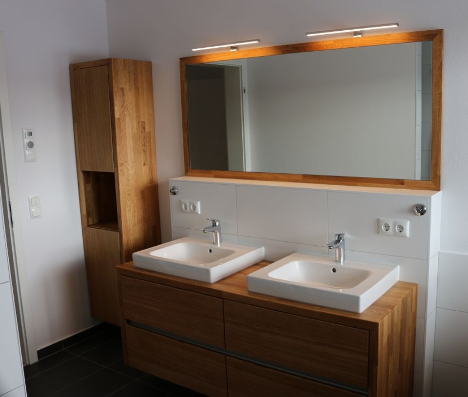 Badezimmeransicht: zwei weiße Waschbecken, darunter Schubladen aus hellem Holz, darüber ein Spiegel