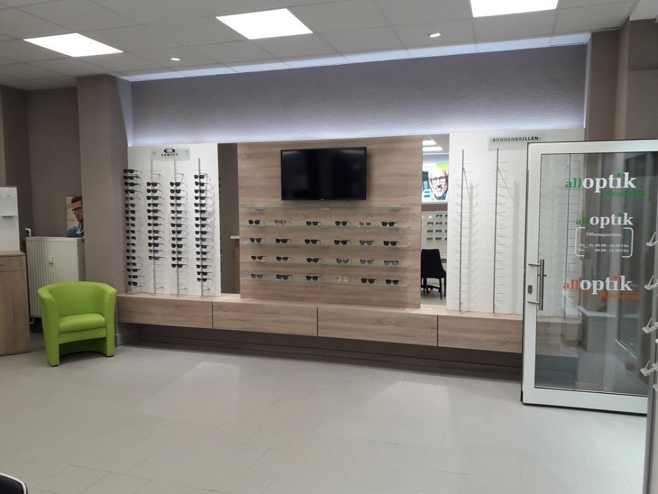 Innenansicht Optiker, vorne rechts der Tresen, vorne links ein Brillenschaukasten, hinten Wand mit Brillen und Treppe nach oben