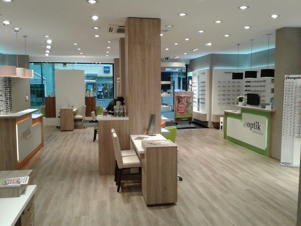 Innenraum Optiker: links und rechts Verkaufstresen, in der Mitte Tisch und Stuhl zur Beratung, Holzeinrichtung