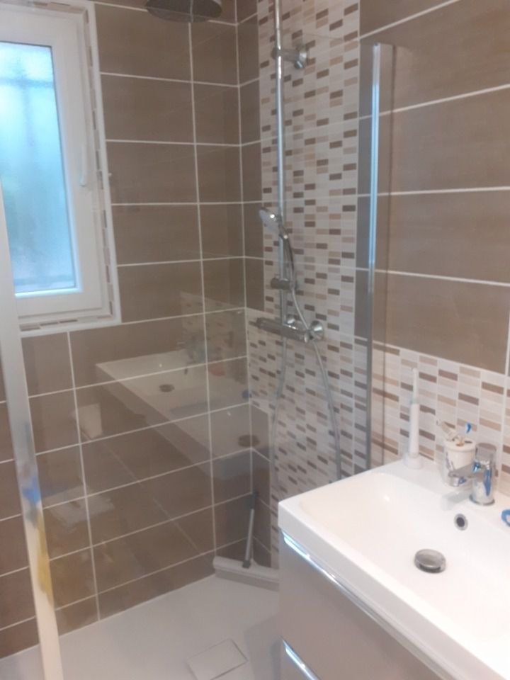 Salle de bains avec douche carrelée, paroi vitrée, fenêtre et meuble vasque.