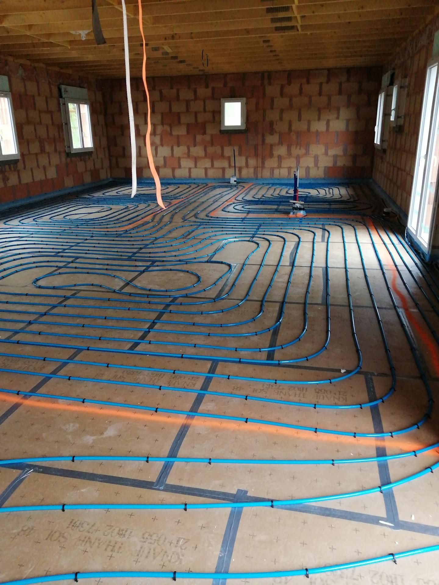 Intérieur d’une maison en construction, avec des tuyaux de chauffage au sol posés sur l’isolant.