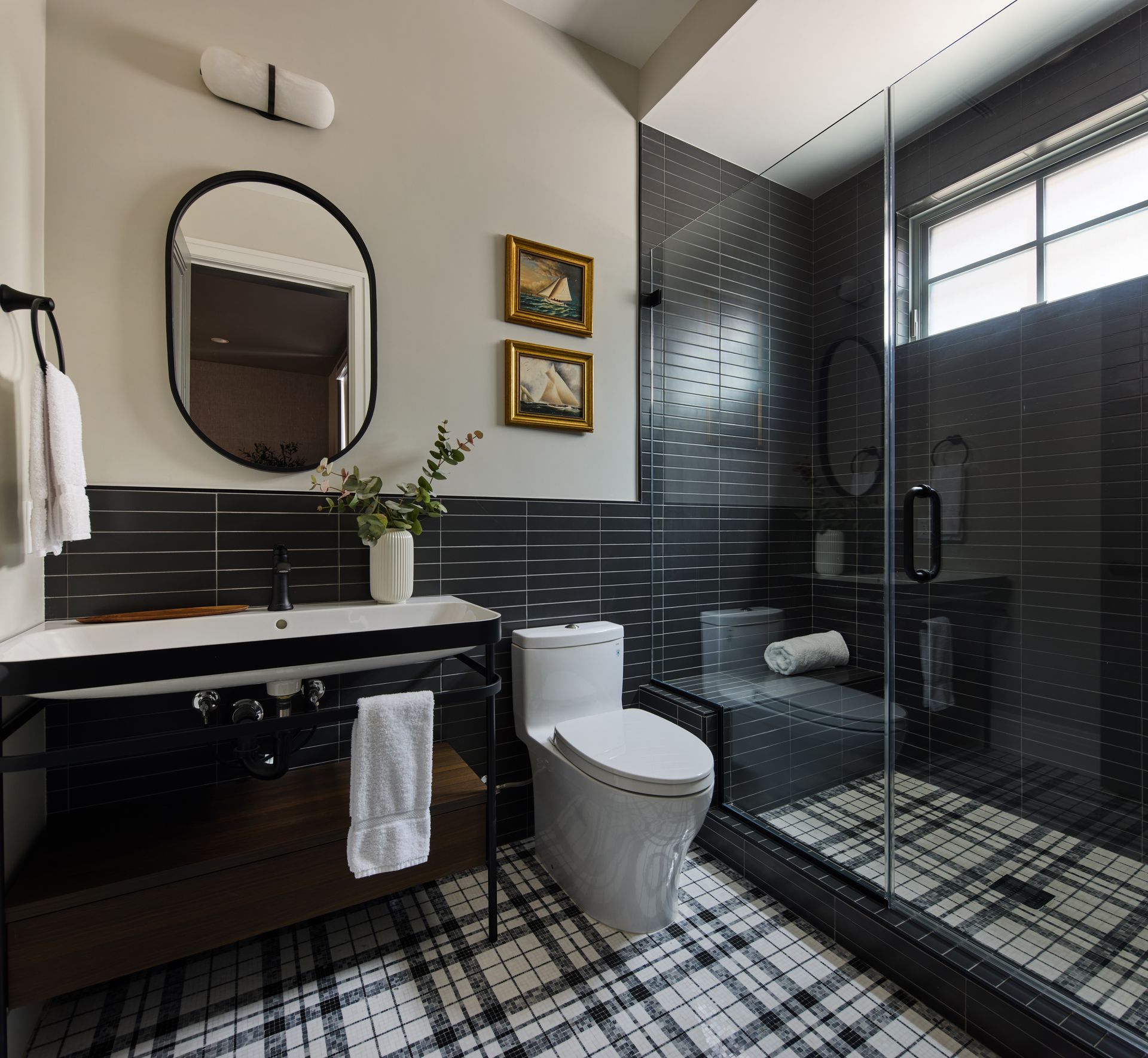 Salle de bains avec douche vitrée, toilettes, meuble-lavabo et miroir rond.