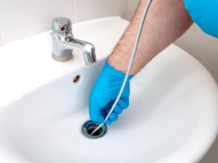 Une main gantée utilise un furet pour déboucher un lavabo.