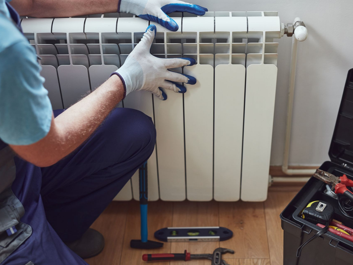 Personne en train d’installer un radiateur, avec des outils posés au sol.