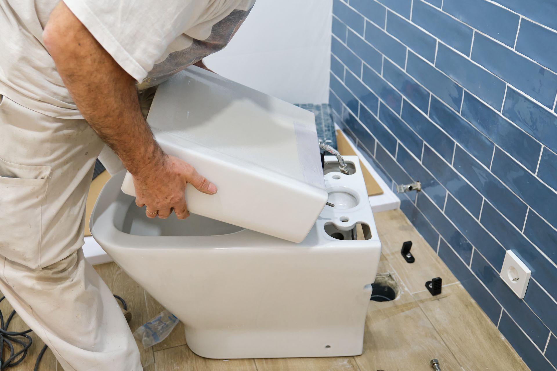 Un ouvrier installe des toilettes dans une salle de bains aux murs carrelés.