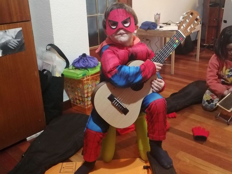 Un niño disfrazado de Spiderman toca la guitarra.