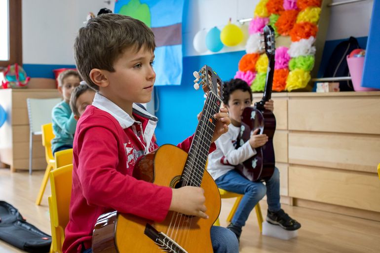 Un niño pequeño está tocando una guitarra en un aula con otros niños.