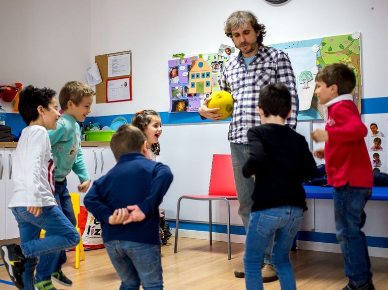 Un grupo de niños está de pie alrededor de un hombre que sostiene una pelota amarilla.