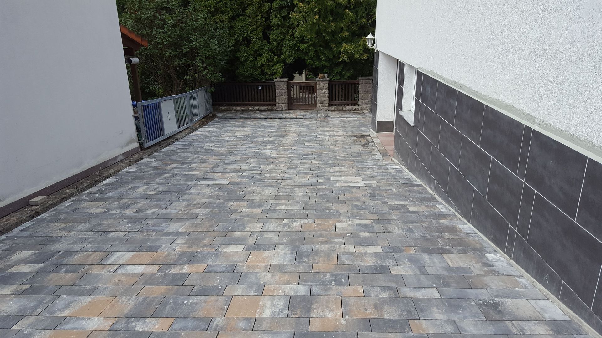 Gepflasterte Auffahrt zwischen zwei Gebäuden, die zu einem umzäunten Hinterhof führt.