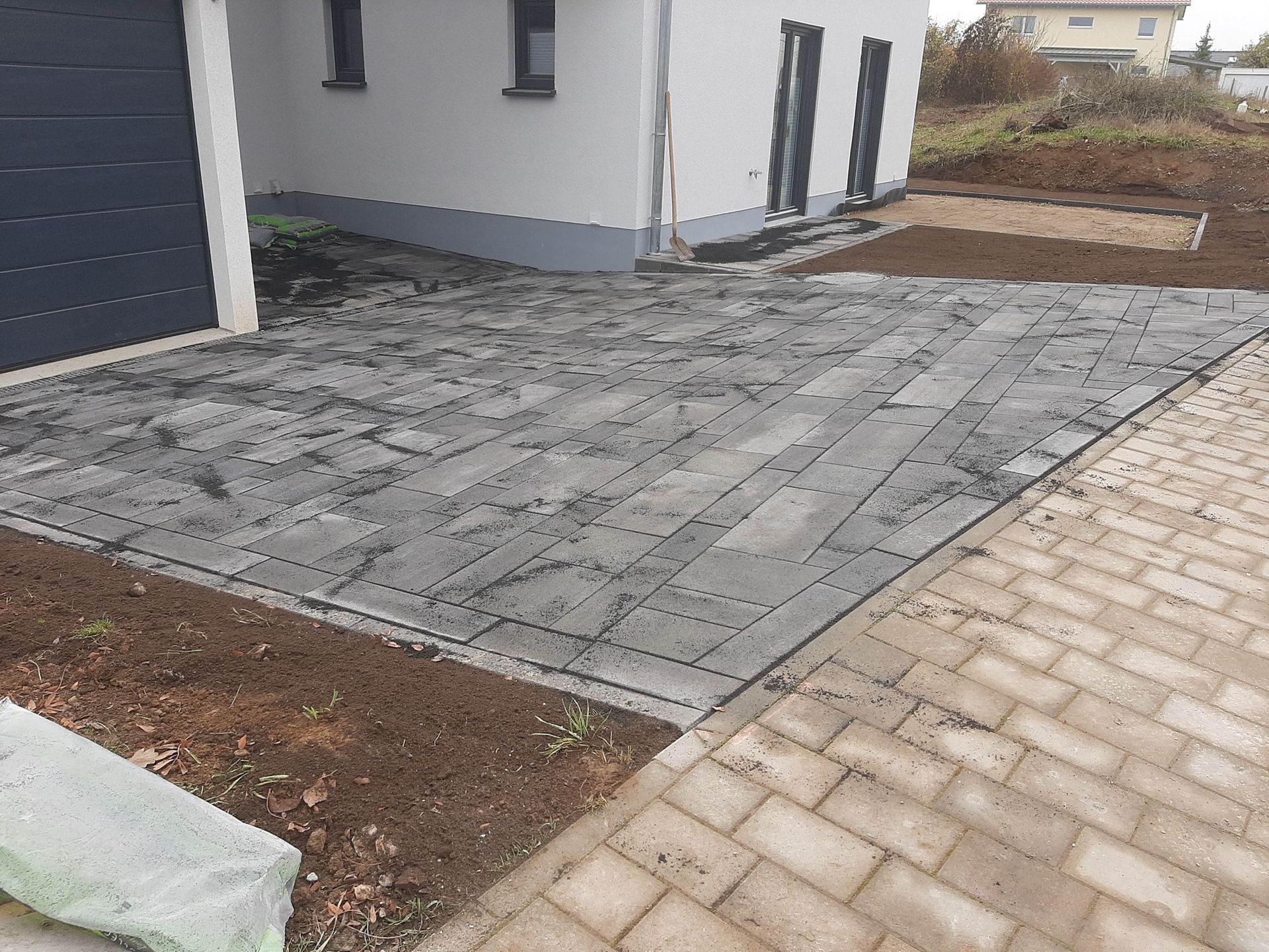 Frisch gepflasterte graue Auffahrt neben einem Haus, gesäumt von einem Gehweg aus Ziegeln und Erde.