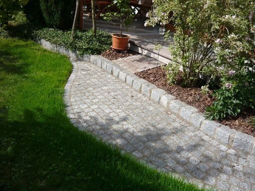 Ein Steinpfad schlängelt sich durch einen Garten mit grünem Gras und Sträuchern.