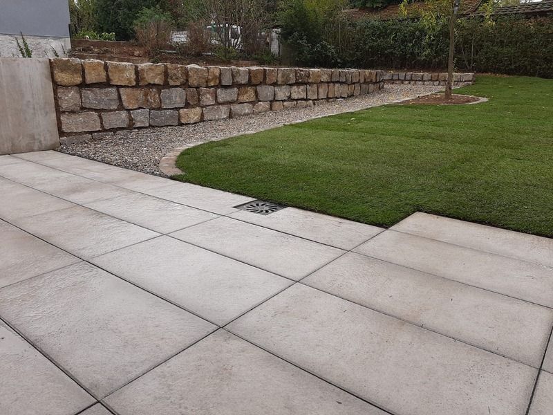 Steinterrasse mit Rasen, Kiesweg und Steinstützmauer.