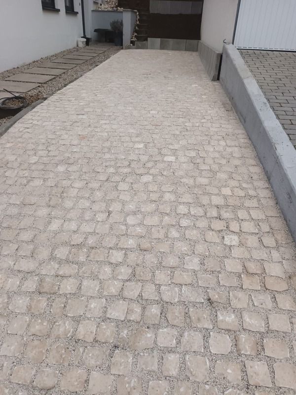 Zu einem Gebäudeeingang führende gepflasterte Auffahrt mit grauen Pflastersteinen und einem Steinweg an der Seite.
