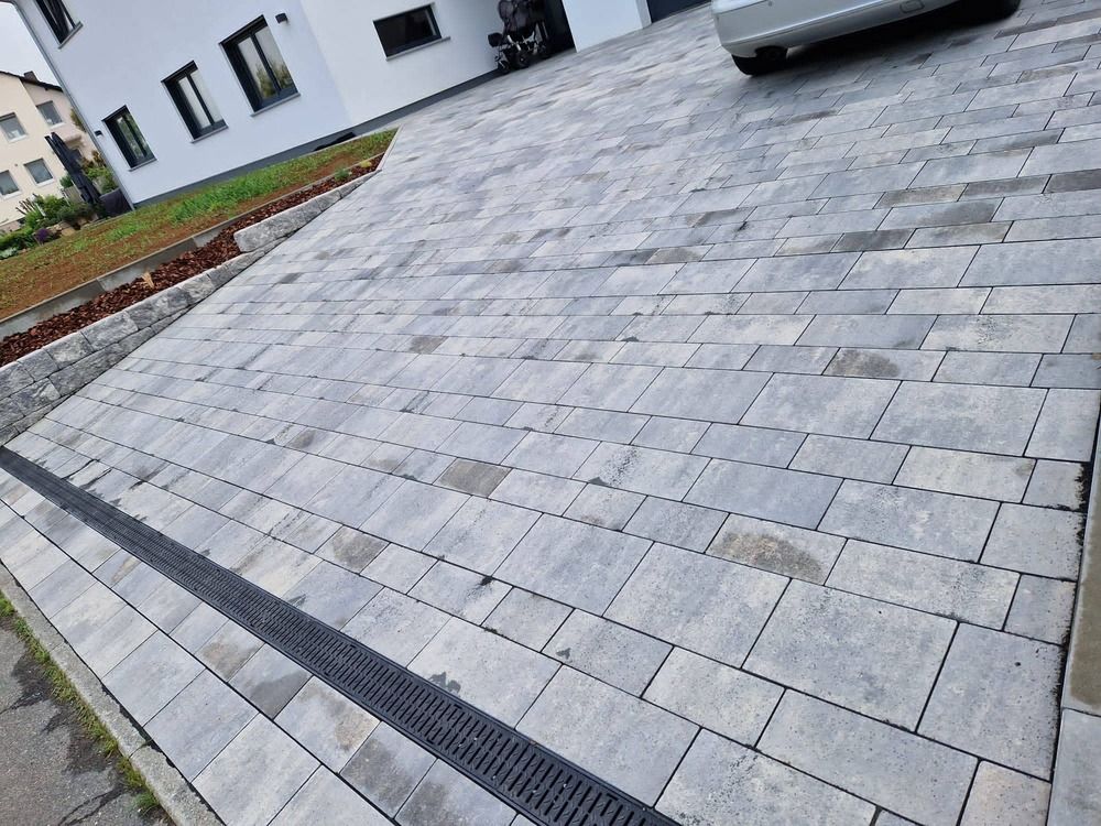 Graue Ziegelauffahrt, die zu einem weißen Gebäude führt, auf dessen Dach ein Auto geparkt ist.