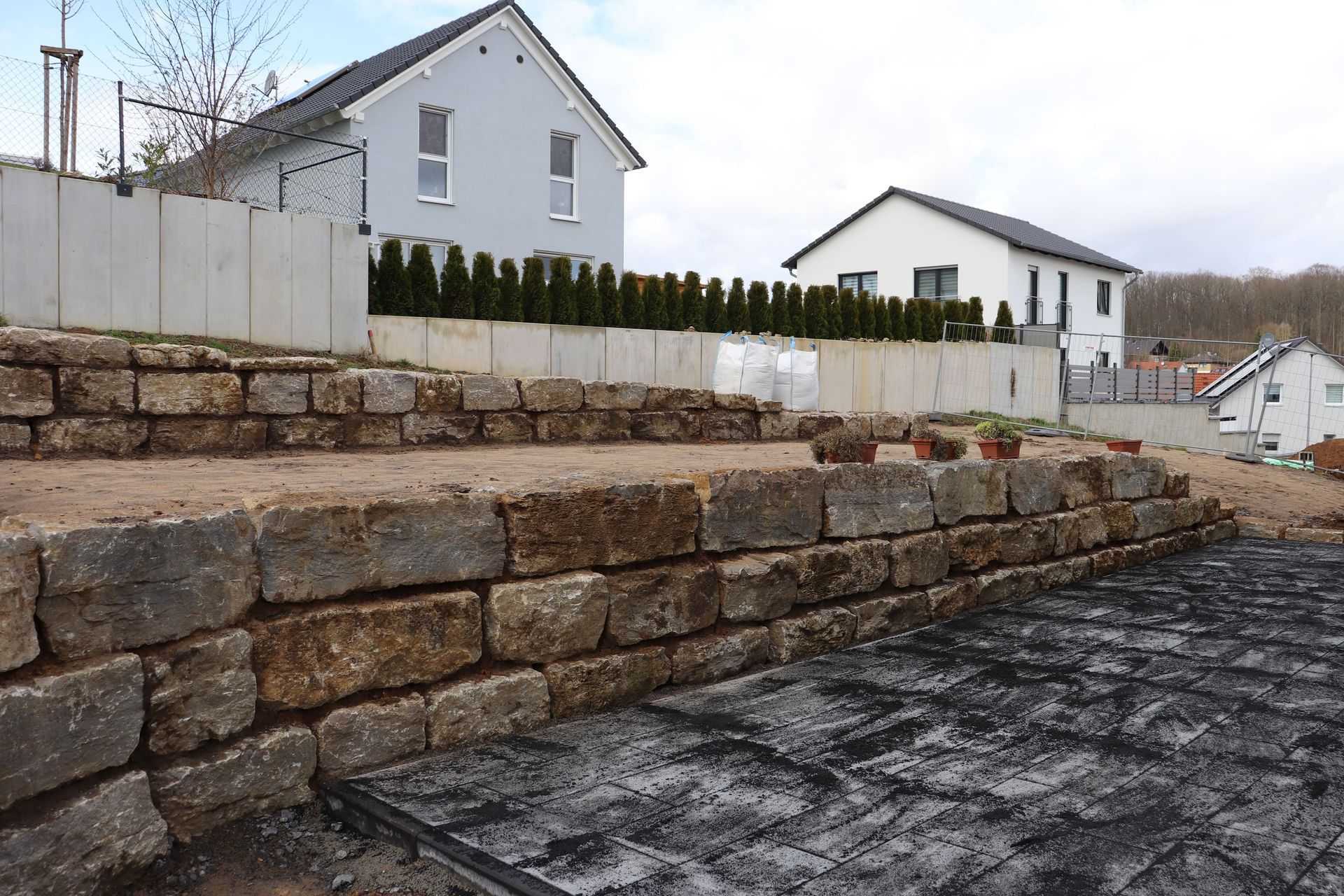 Steinerne Stützmauern vor den Häusern, mit einem leeren Grundstück und bewölktem Himmel.