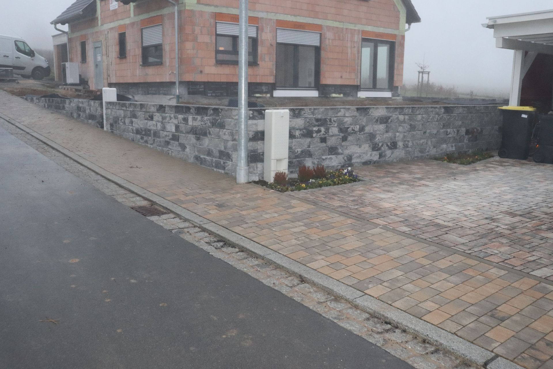Ein im Bau befindliches Haus mit einer Steinmauer und einer gemauerten Auffahrt an einem nebligen Tag.