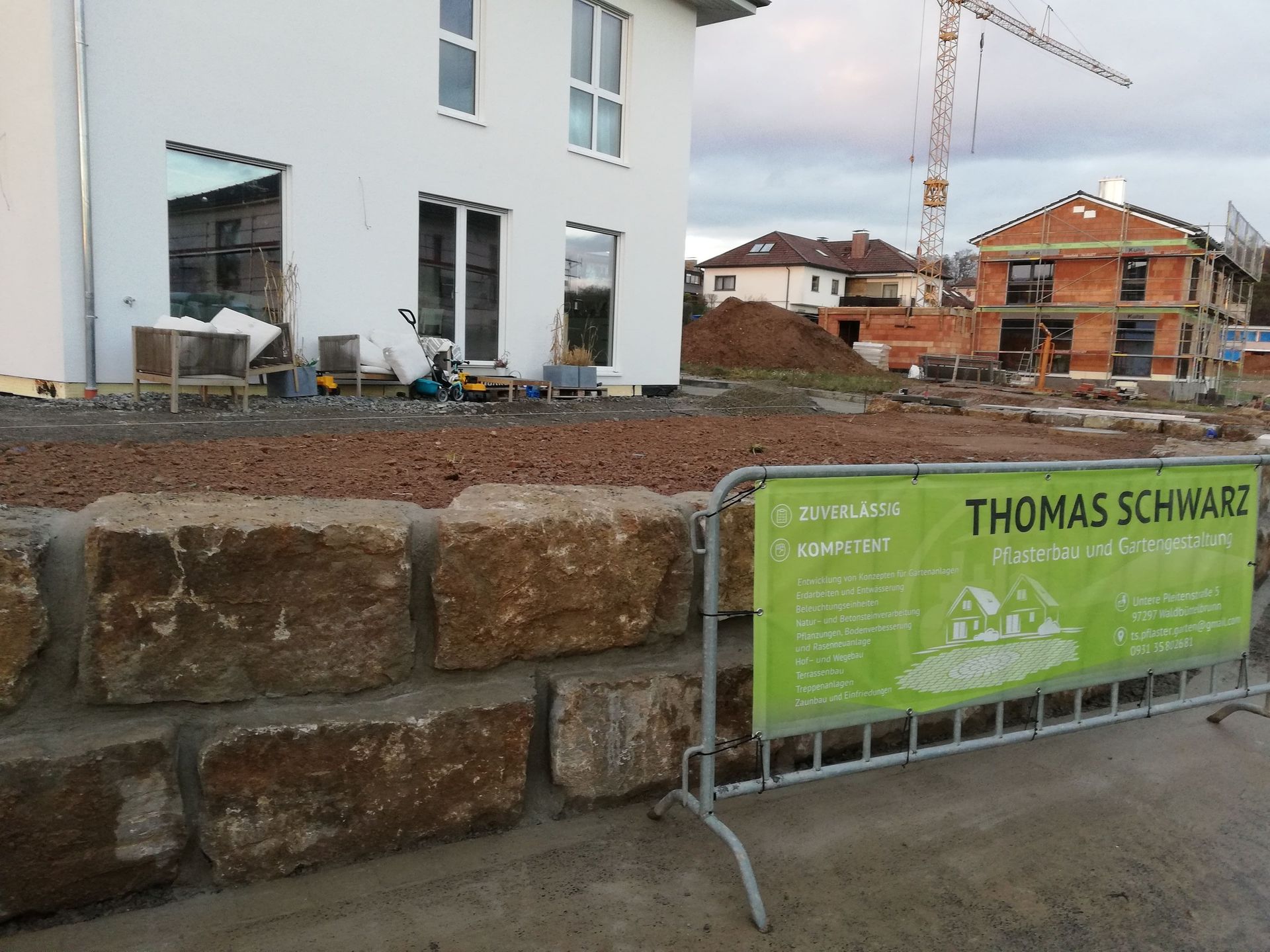 Baustelle mit Häusern, Kran, Felswand und einem Banner für Thomas Schwarz.