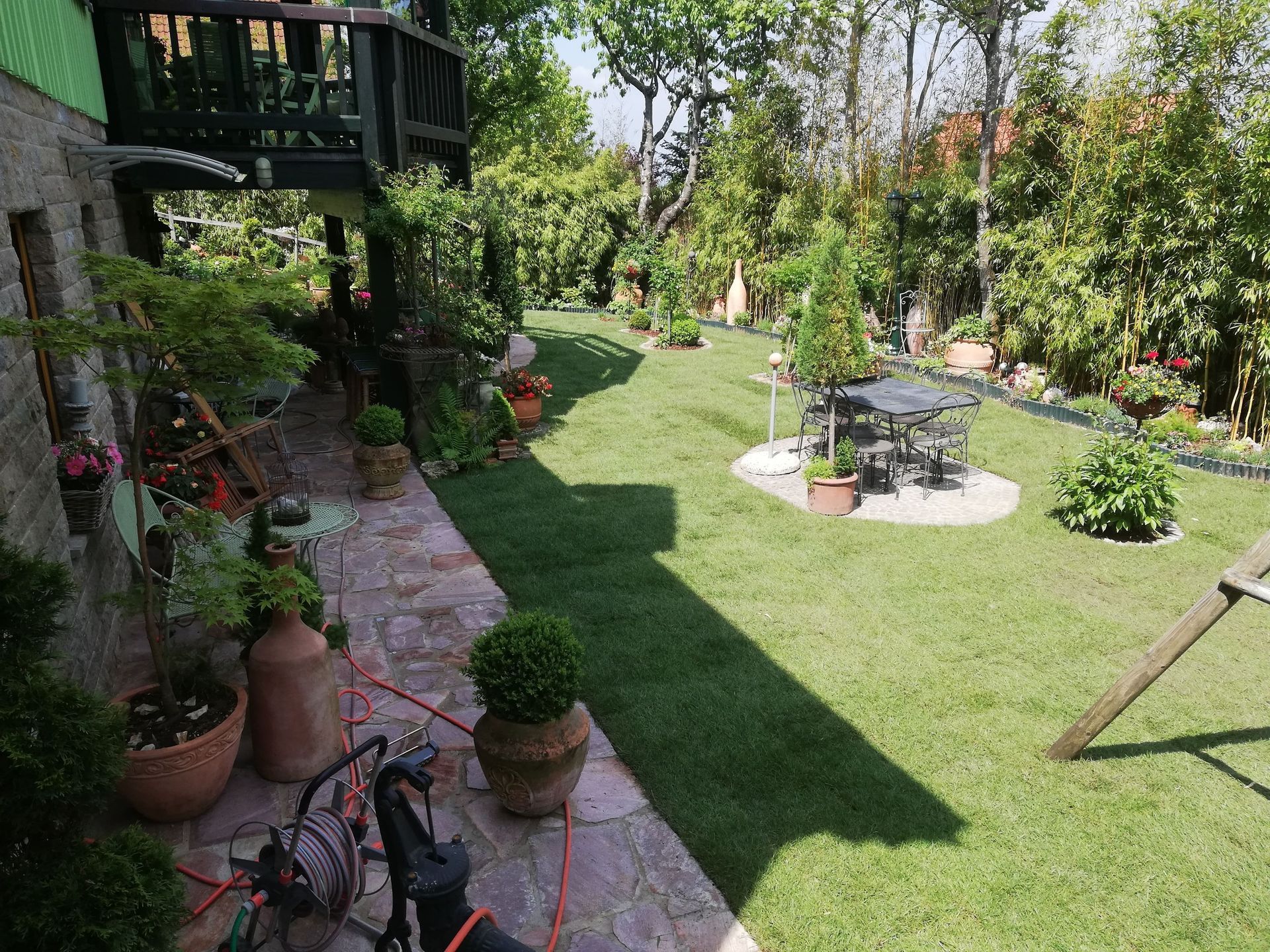 Hinterhof mit üppigem grünen Rasen, Steinterrasse, Holzdeck und verschiedenen Topfpflanzen.