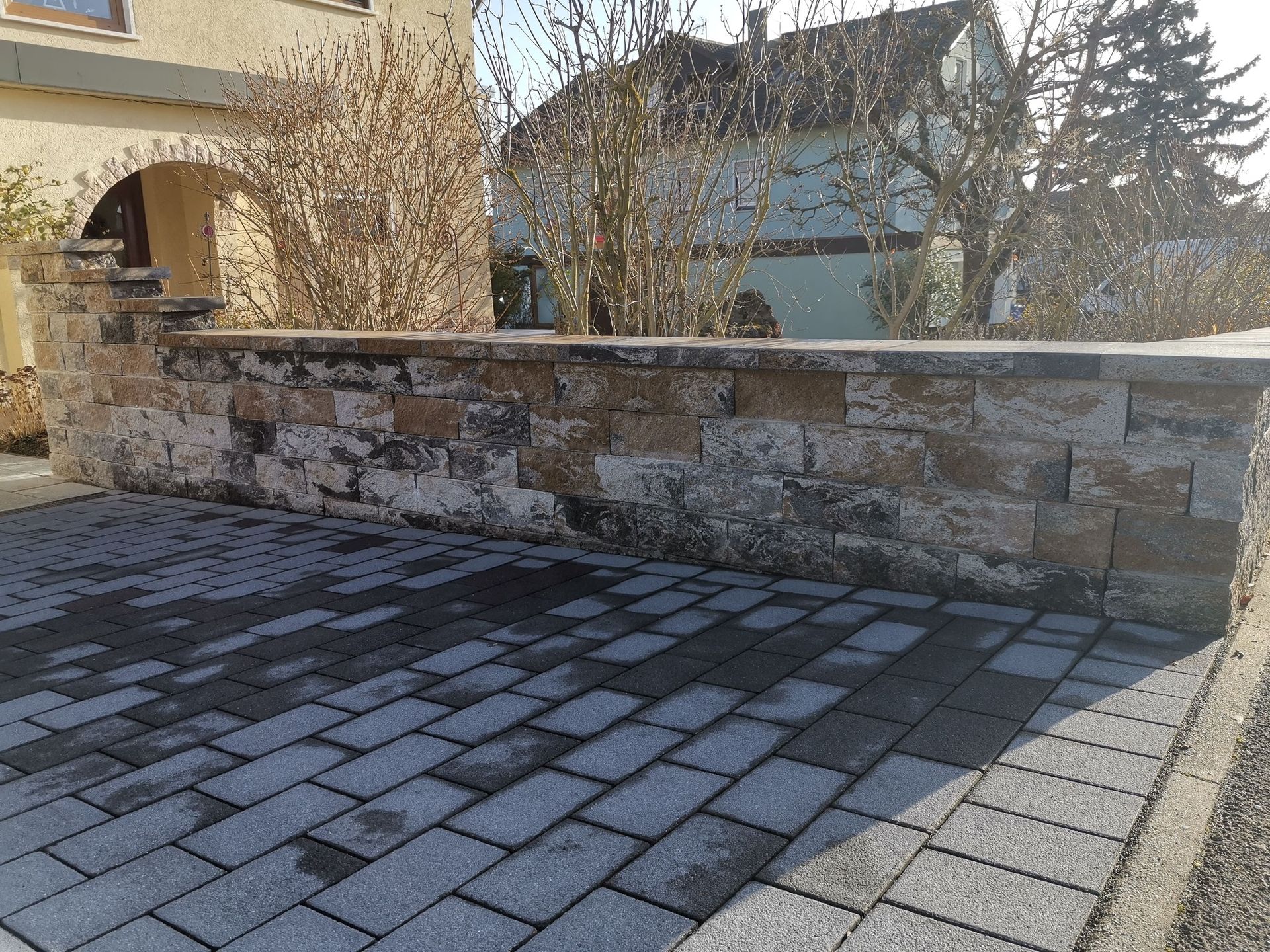 Steinmauer vor einem Haus mit Ziegelpflaster.